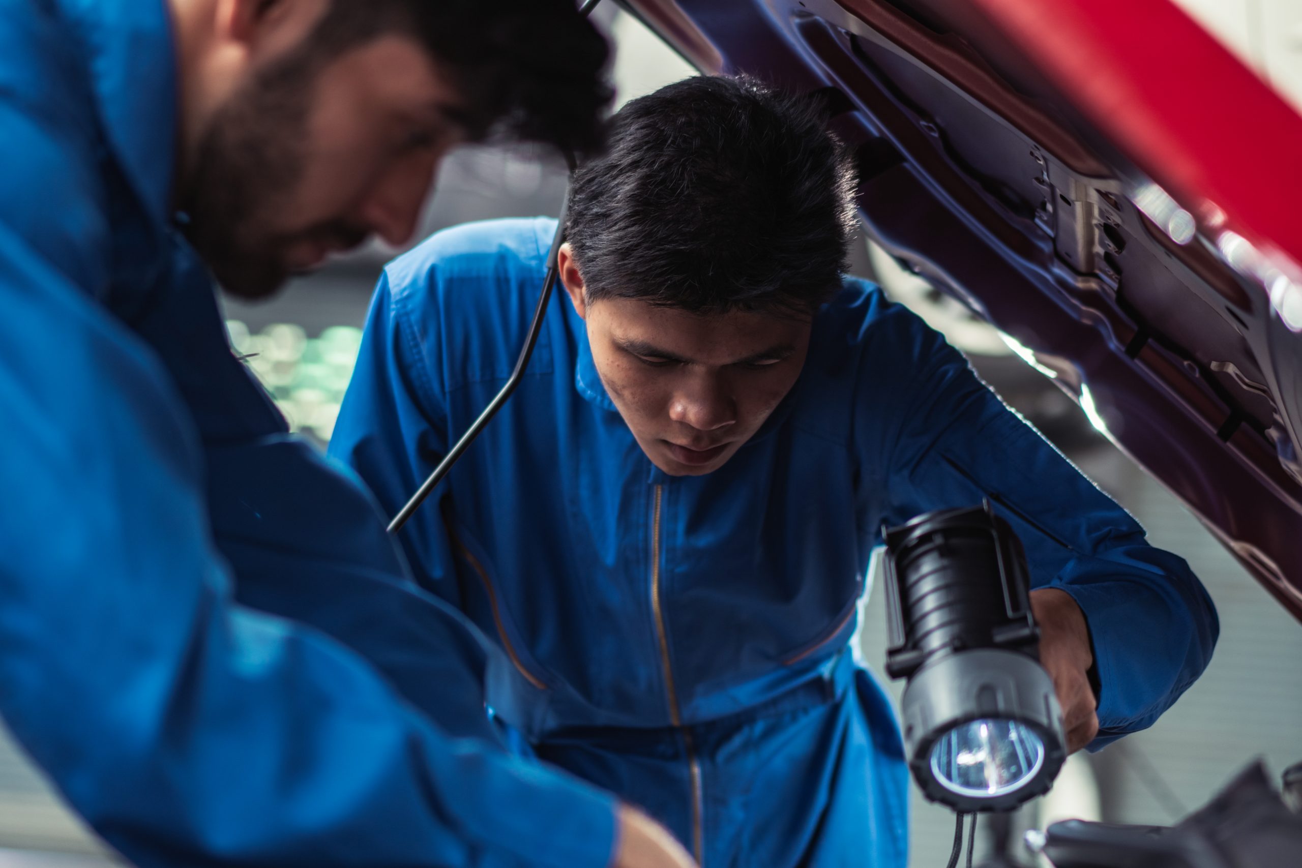 mechanic shining flashlight to help colleagues repairing car eng - Avigauto Recambios